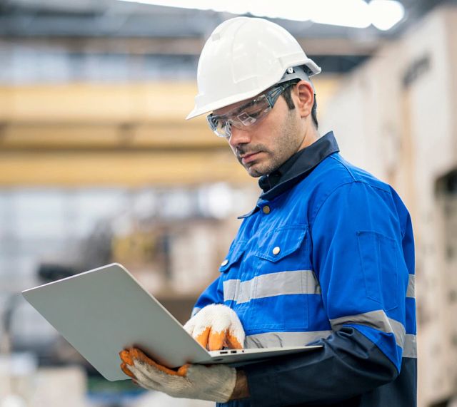 Factory worker with hardhat looking at laptop on factory floor